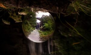 A crystal ball capturing a vivid reflection of a waterfall in a lush green landscape, embodying tranquility and nature.