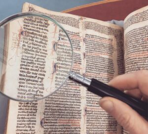 A hand holding a magnifying glass over an antique book page, revealing intricate text and design.