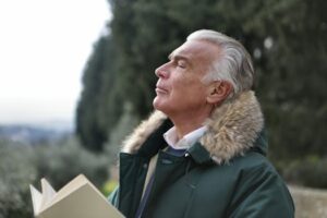 Senior man with white hair, eyes closed enjoying fresh air in Tuscany's natural setting.