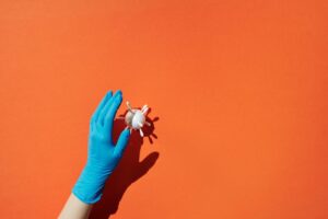 A blue gloved hand reaches for a virus model on a striking orange background, symbolizing caution.