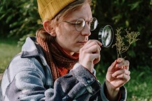 A botanist examines a plant with a magnifying glass in an autumn garden setting.